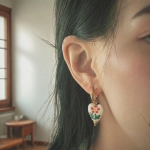 Golden hoop earrings with heart-shaped ceramic floral pendants on model ear