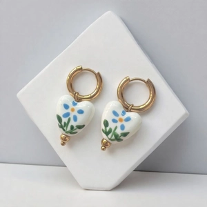 Close-up of heart ceramic drop earrings with blue floral pattern and 18K gold-plated hoops