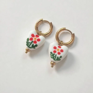 Detail view of 18K gold-plated hoops with white heart ceramic floral pendants