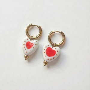 Detail of 18K gold plated hoop earrings featuring ceramic heart pendants with red patterns