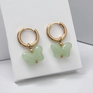 Detail view of 18K gold plated hoop earrings with light green butterfly charms on display