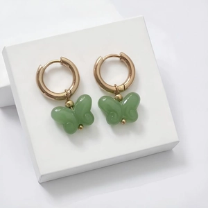 Detailed shot of gold-plated hoop earrings featuring light green butterfly charms on white