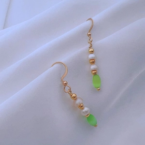 Detailed close-up of gold dangle earrings with baroque pearls and emerald green beads