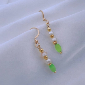 Detail view of long tassel pearl earrings with green beads on white fabric