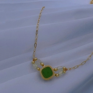 Macro detail of golden necklace with green square pendant on white draped fabric
