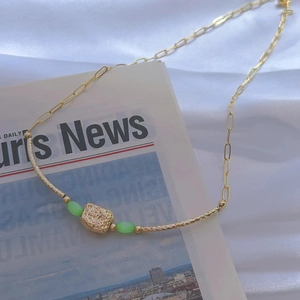 Macro detail of gold paperclip chain necklace with green cat-eye bead and textured pendant
