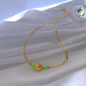 Detail of gold heart pendant necklace with green cat-eye beads on white silk