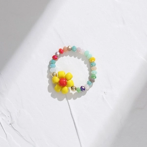 Colorful beaded ring with yellow flower charm on minimalist white textured stone