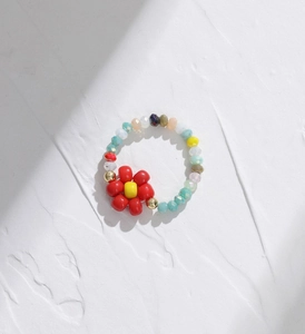 Detail shot of multi-color beaded elastic ring featuring a red floral charm on white panel