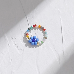 Close-up of handmade colorful seed bead ring with blue flower design on textured surface