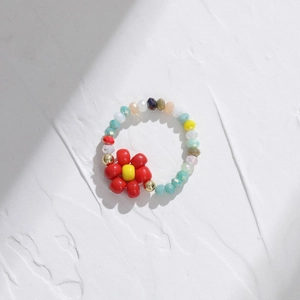 Handmade colorful beaded flower ring with red petals and gold accents on white texture