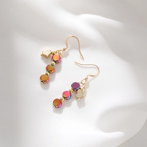 Detail of gold heart earrings with iridescent faceted beads on white silk fabric