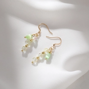 Detail of handmade drop earrings featuring pale green cat eye stone on white silk fabric