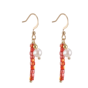 Macro detail of gold hook earrings featuring red square beads and a white freshwater pearl