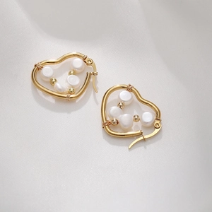 Close-up of heart-shaped gold earrings with wrapped pearls on white silk
