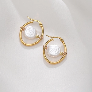 Macro detail of gold hoop earrings with white baroque pearls on white silk background