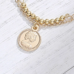 Double-layered 14K gold-plated bracelet with vintage coin pendant on white wood surface