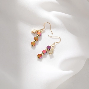 Handmade colorful drop earrings with iridescent beads and golden heart charms on white fabric