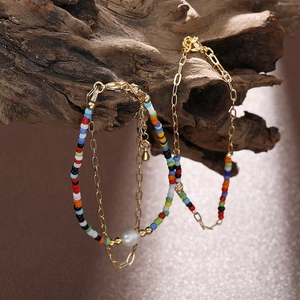 Dettaglio di bracciale boho con perline colorate, catena a graffetta dorata e perla