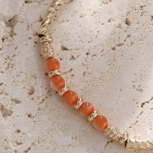 Bracelet doré à perles œil de chat orange avec des tubes métalliques à texture ciselée