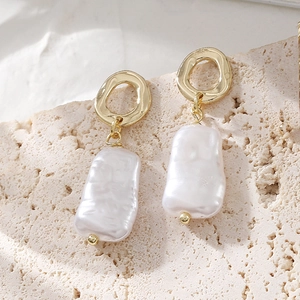 Boucles d'oreilles perles baroques et anneaux dorés sur fond de pierre texturée