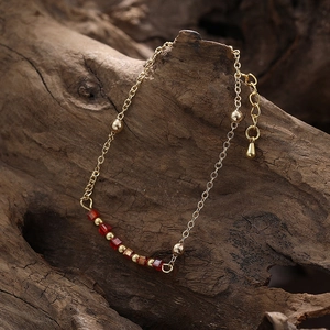 Bracelet bohème doré avec perles rouges carrées sur une surface en bois texturée