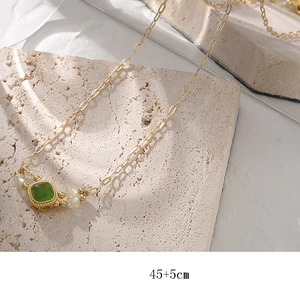 Vintage emerald pendant necklace with square gemstone and gold chain on travertine