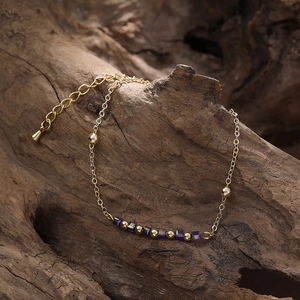 Détail d'un bracelet doré avec perles bleues présenté sur un fond en bois naturel