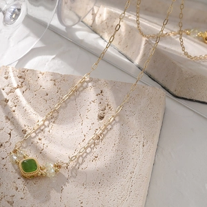 Vintage gold necklace with emerald green pendant on a textured stone surface