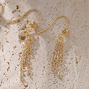 Elegant gold tassel chain earrings with zircon on a natural beige stone background