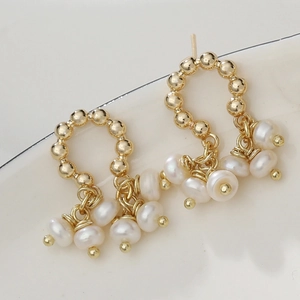 Elegant gold bead hoop earrings with hanging freshwater pearls on a ceramic dish
