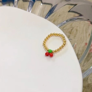 Dettaglio dell'anello elastico con perline dorate e ciondolo a forma di ciliegia