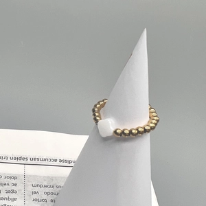 Detail of 18K gold stainless steel beaded ring with a white clover shell charm on a stand