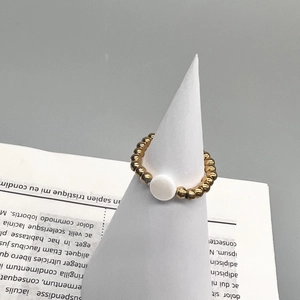 Macro detail of 18K gold stainless steel beaded ring with white shell charm on stand