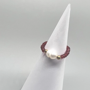 Detail of a handmade stretch ring with white freshwater pearls and red faceted glass beads