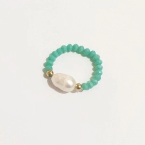 Detailed top view of handmade elastic ring with a white baroque pearl and green beads