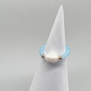 Detail of a light blue beaded stretch ring with a freshwater pearl on a white cone stand