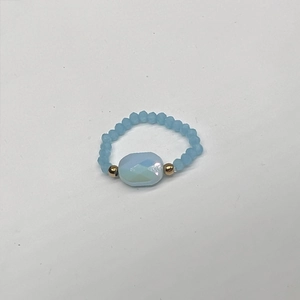 Macro detail of sky blue beaded elastic ring with gold spacers and blue faceted oval stone