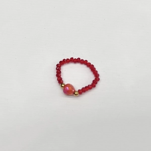 Macro detail of elastic beaded ring featuring red faceted beads and pink gradient centerpiece