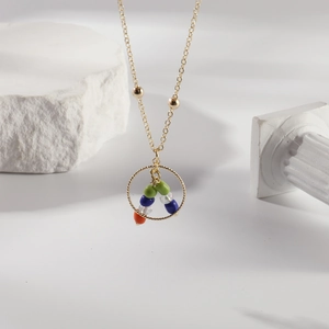 Minimalist stainless steel necklace with gold beads and colorful stone pendant on white stone