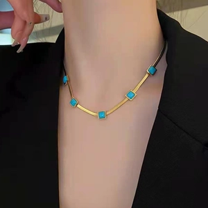 Collana piatta a serpente dorata con pietre turchesi indossata su un blazer nero