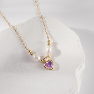Collier de perles dorées avec pendentif cœur violet sur une pierre blanche texturée