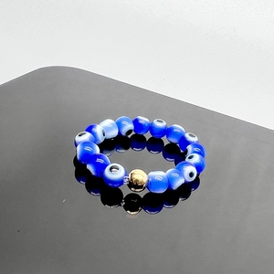 Close-up of blue glass evil eye beaded elastic ring with a central gold metal accent