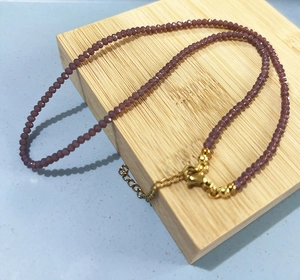 Detail of purple faceted crystal beads necklace with golden lobster clasp on bamboo stand