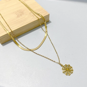 Detail of layered gold snake chain and cable necklace featuring a spider web pendant
