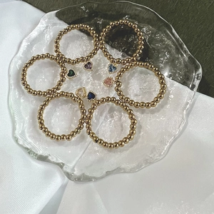 7-piece set of golden beaded elastic rings with colorful heart pendants in a glass tray