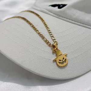 Halloween pumpkin ghost pendant on a gold Figaro chain necklace over a white hat