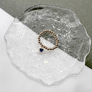 Close-up of golden beaded stretch ring with a hanging heart-shaped blue gemstone charm