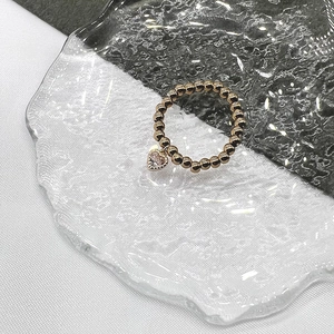 Close-up of golden beaded ring with a heart-shaped zircon pendant on glass surface