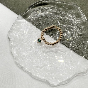 Detail of beaded gold ring featuring a heart-shaped green emerald pendant on glass